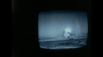 Image from a black-and-white home movie of a nuclear explosion on a TV set.