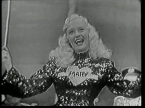 Black and white still from an episode of Super Circus showing Mary Hartline conducting the Super Circus orchestra.